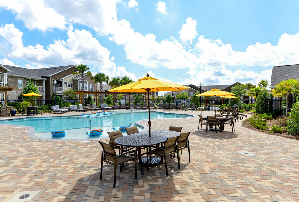 Patio tables and chairs with yellow table umbrellas lining the outdoor pool at Villas at Park Avenue