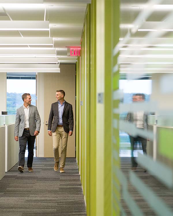 Two employees walk down an office hallway